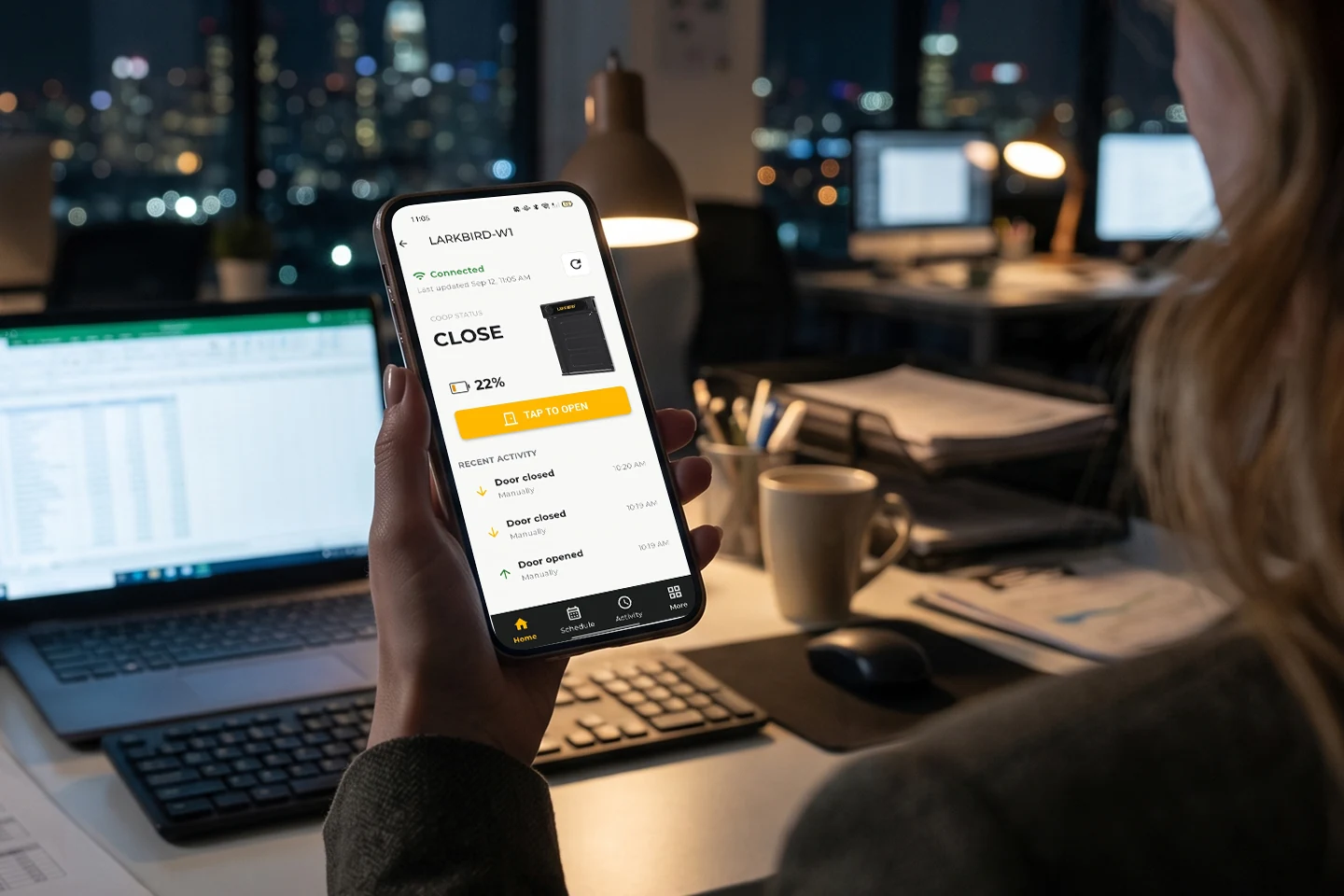 Someone working late in an office checks the coop app on their phone; the door status reads CLOSE while city lights shine outside.