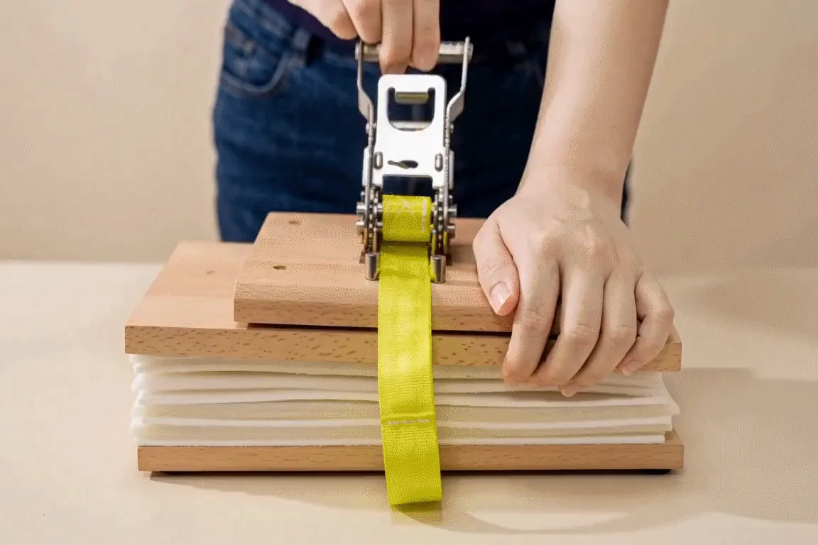 Animated: one hand pulling the ratchet handle to tighten the strap while the other steadies the pin end.